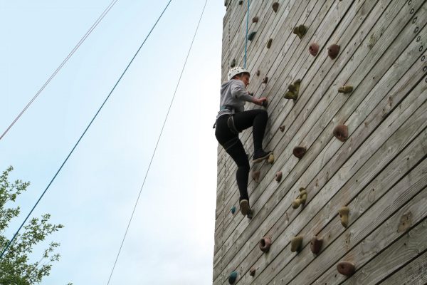 Girl climbing a climbing tower with helmet on and safety harness